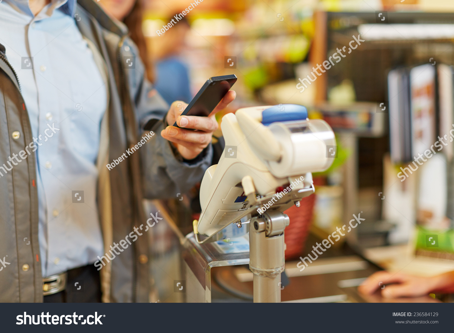 Man paying wireless with his smartphone at supermarket checkout