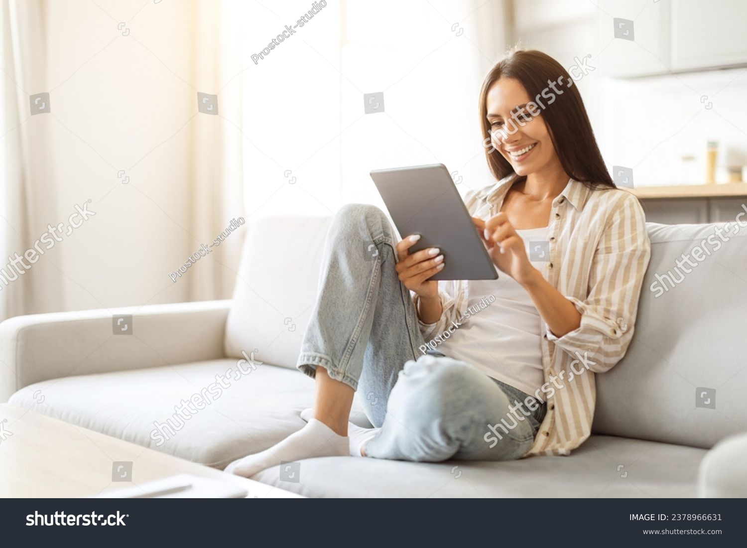 Smiling beautiful woman relaxing with digital tablet on couch at home ...