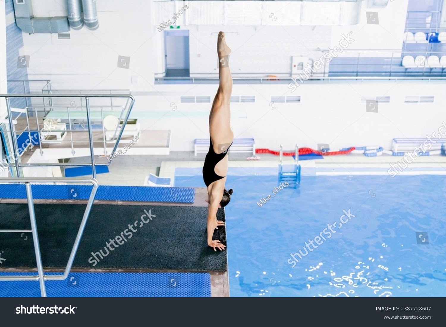 a girl stands on her hands on the edge of a springboard preparing to jump into the water