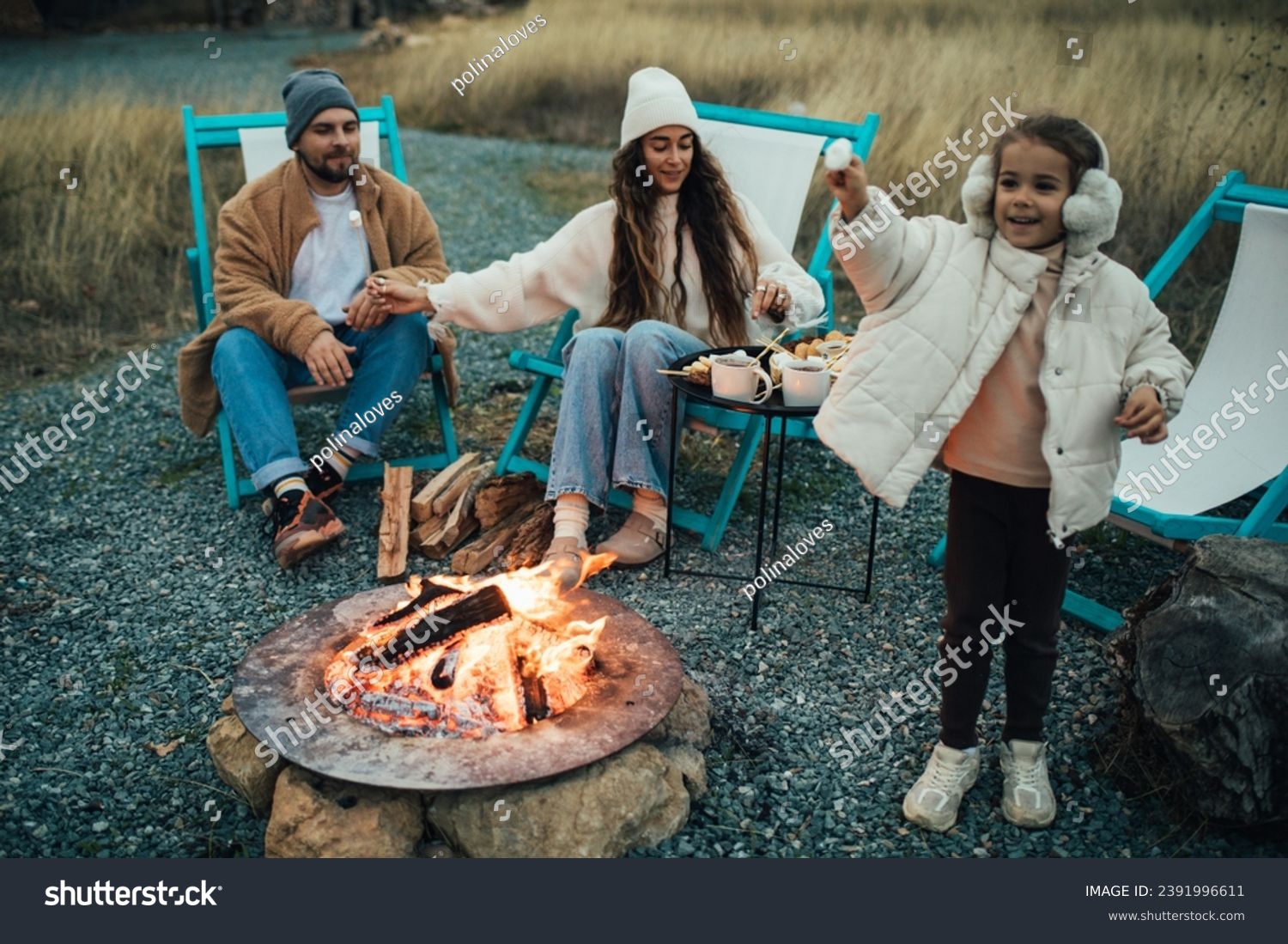 Happy family roasting marshmallow sitting by the fire outdoors.