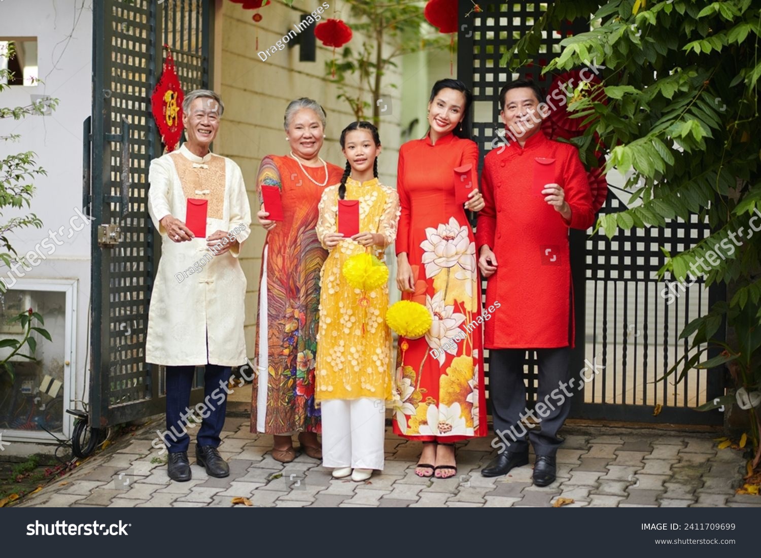 Happy family showing red envelopes with lucky money when standing in front of house gates