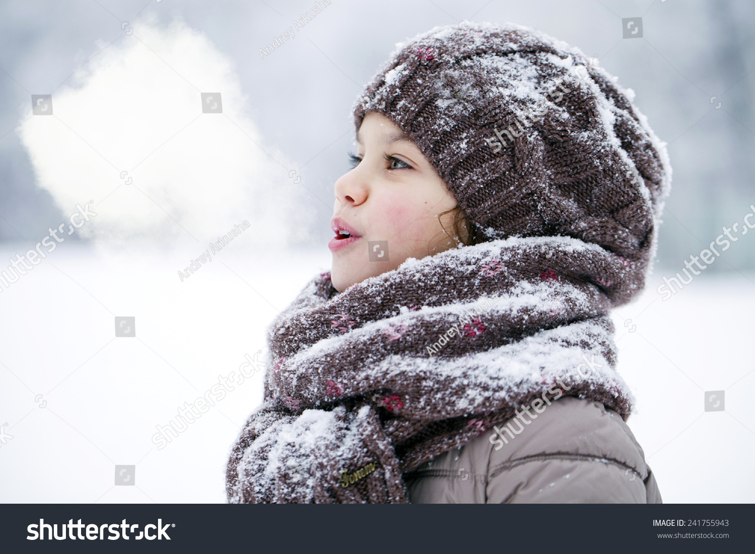 Close-up portrait of a little girl in brown jacket and knit scarf and hat on a background of a snow park