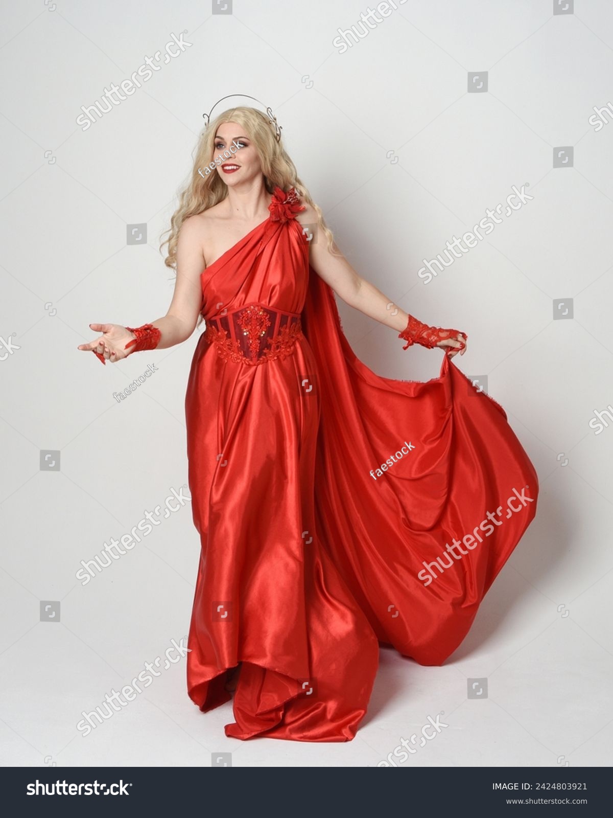 Full length portrait of blonde model dressed as ancient mythological fantasy goddess in flowing red silk toga gown crown. elegant dancing pose with flowing fabric isolated on white studio background