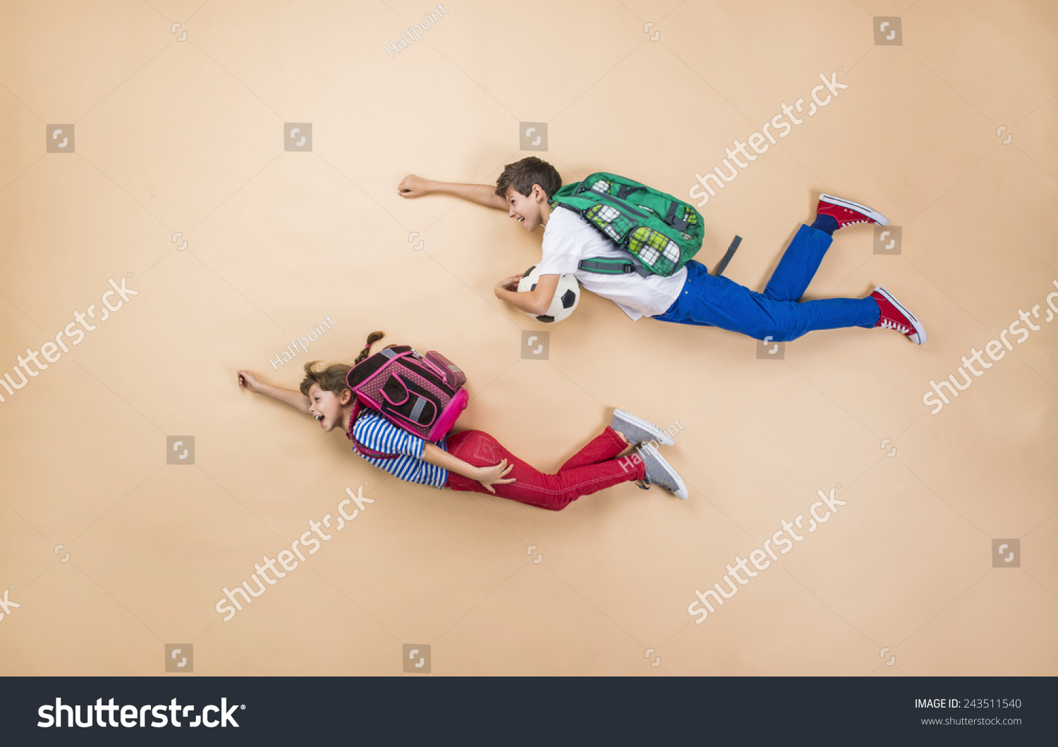 Happy children running to school in a hurry. Studio shot on a beige background.
