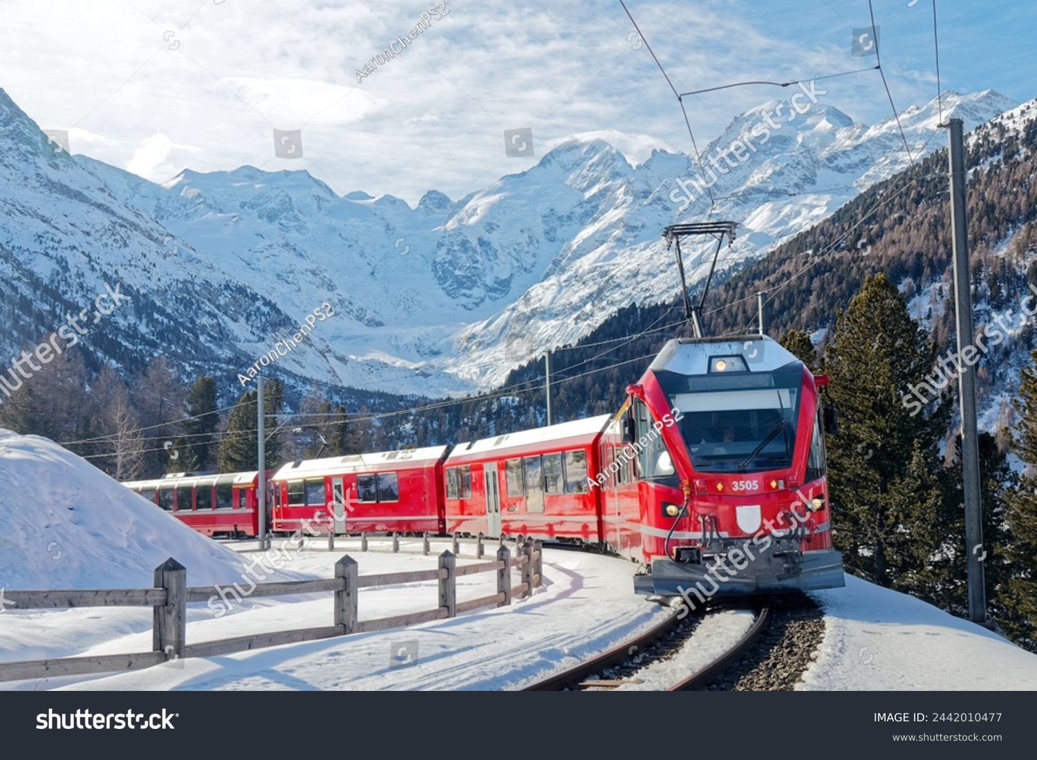 A Bernina Express travels thru Montebello Curve on a sunny winter day with Morteratsch Glacier lying below Piz Bernina and snowy mountains in background in Pontresina Graubünden Switzerland Europe