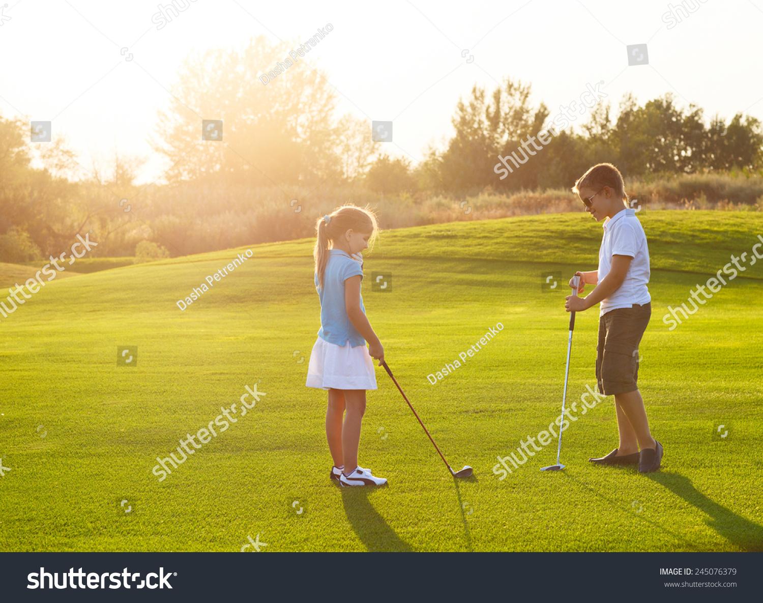 Casual kids at a golf field holding golf clubs. Sunset