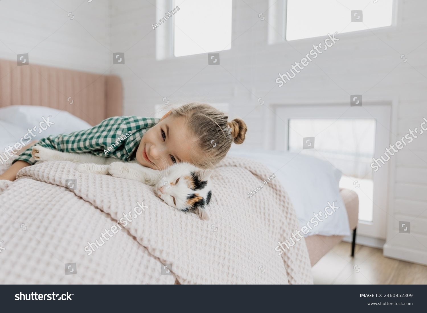 A little blond girl wearing pajamas hugs a domestic cat in her bedroom. The concept of a cozy home morning