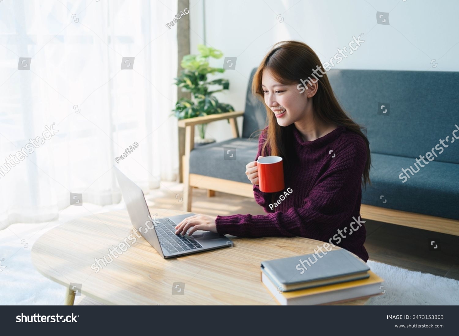 Asian woman is sitting on a table with a laptop and a red coffee mug ...