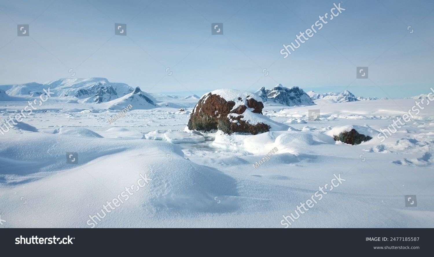 Winter Antarctic landscape in sunny day  blue sky. Desert white land of snow and ice  mountain range in background. Breathtaking travel journey over frozen Antarctica landscape. Low angle drone shot