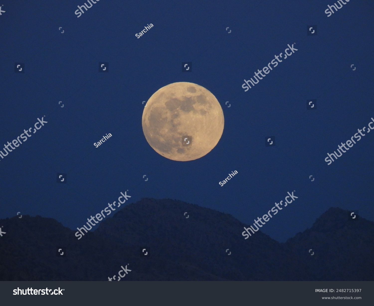 A big  bright full moon shines in the evening sky above dark mountain peaks