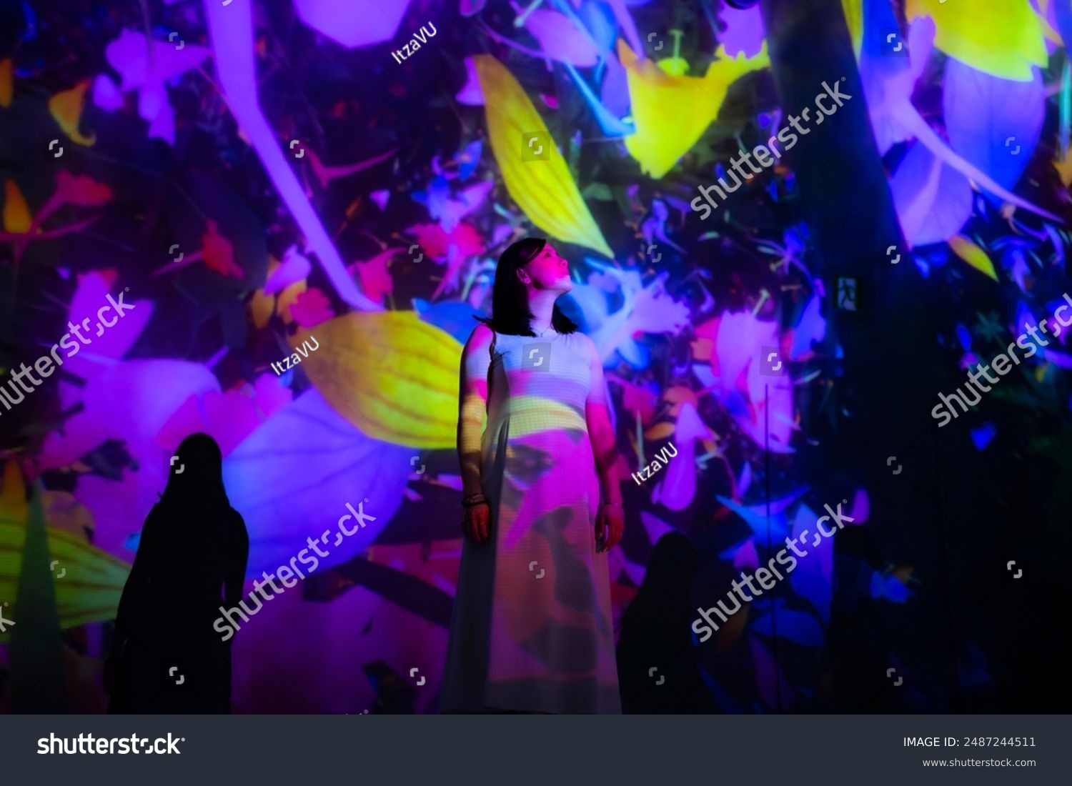 Young Latina woman surrounded by colorful flower projections at TeamLab Tokyo Japon appearing enchanted and mesmerized.