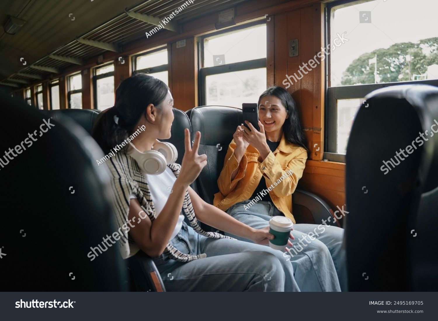 Two female friends are taking pictures with a smartphone while riding a train and having coffee