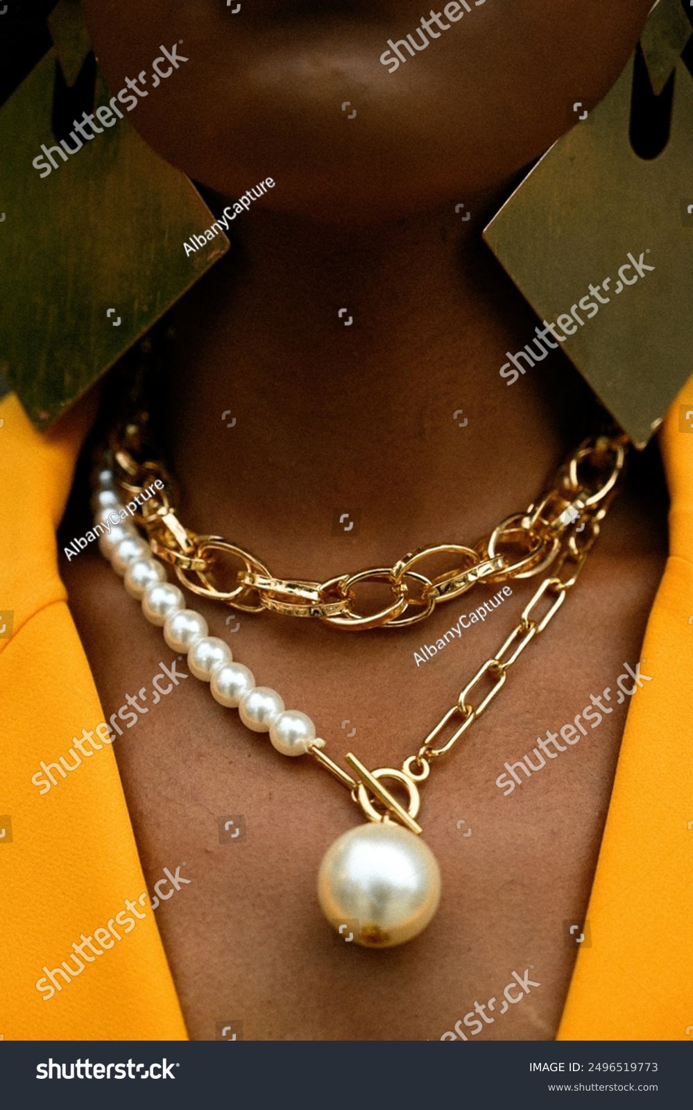 Chicago  IL 05-24-24: a close-up of a person's neck adorned with stylish gold and pearl necklaces  complemented by large geometric earrings and a vibrant yellow outfit.