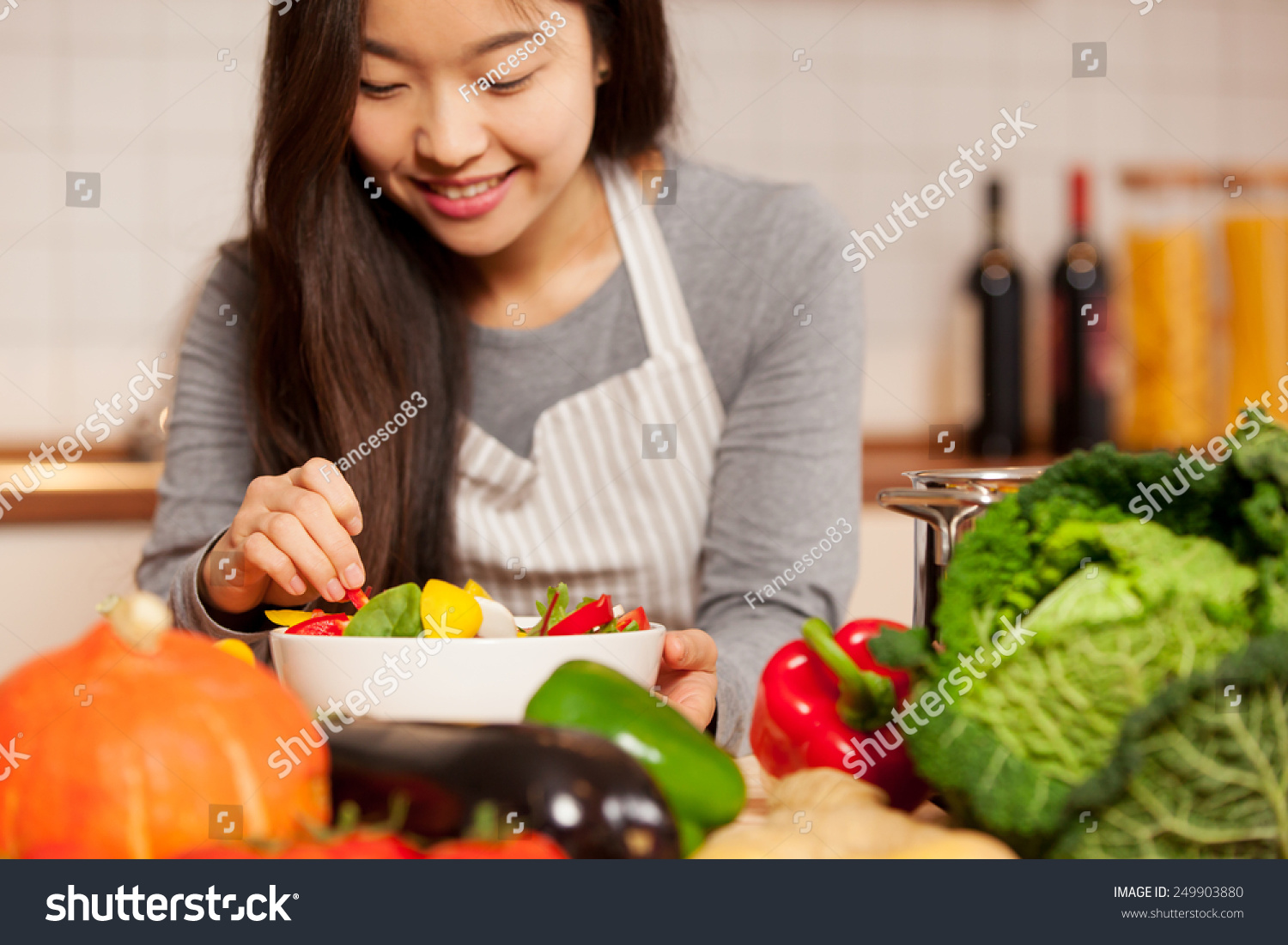 photo of asian young woman composing a colorful salad at home in the kitchen