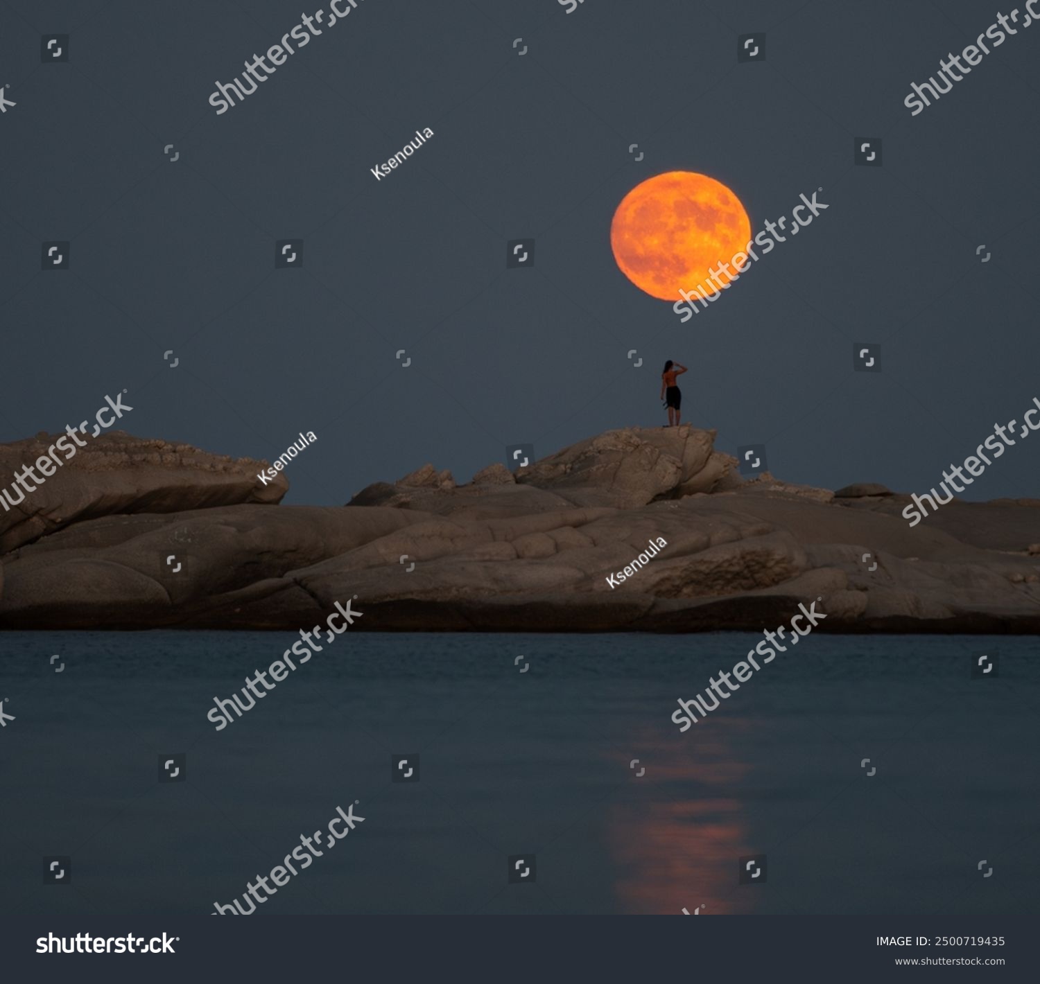 August full moon at the beach with rocks and a girl 