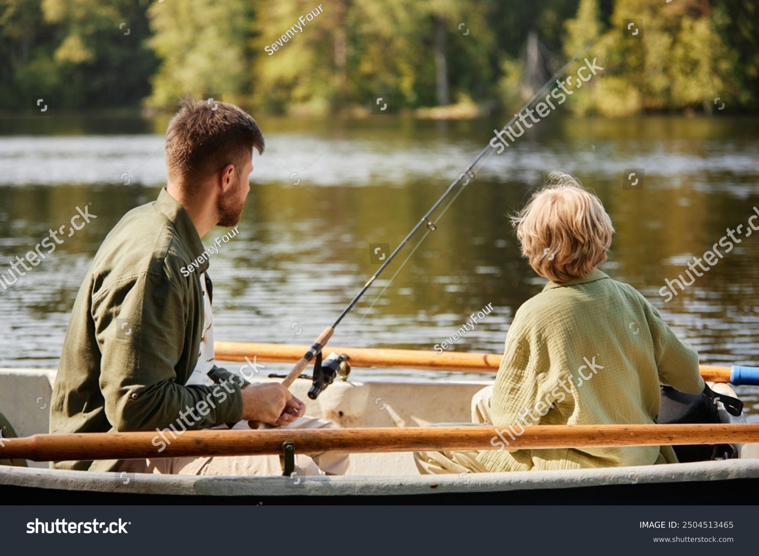 Two individuals enjoying serene fishing experience in a boat on lake surrounded by lush greenery and calm waters providing peaceful scene for outdoor recreation