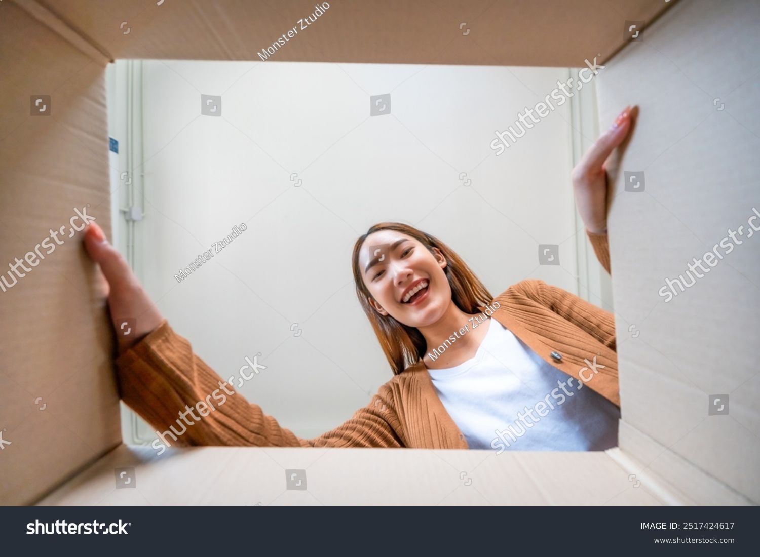 Low angle view of surprised young asian woman unpacking. Opening carton box and looking inside. Packaging box delivery service. Human emotions and facial expression