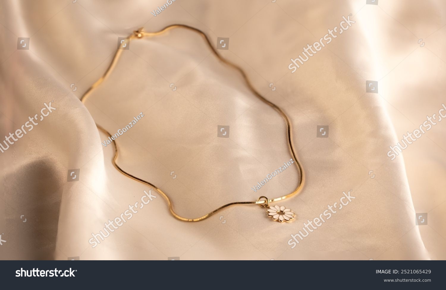 Gold necklace with white flower charm on it on white silk background