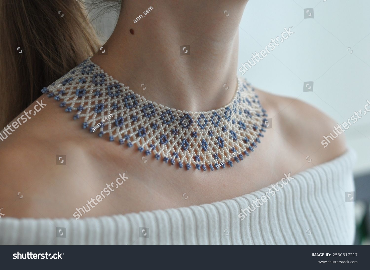 Close-up of a beaded necklace sylianka on a woman’s neck  featuring a delicate net pattern with blue and white beads.