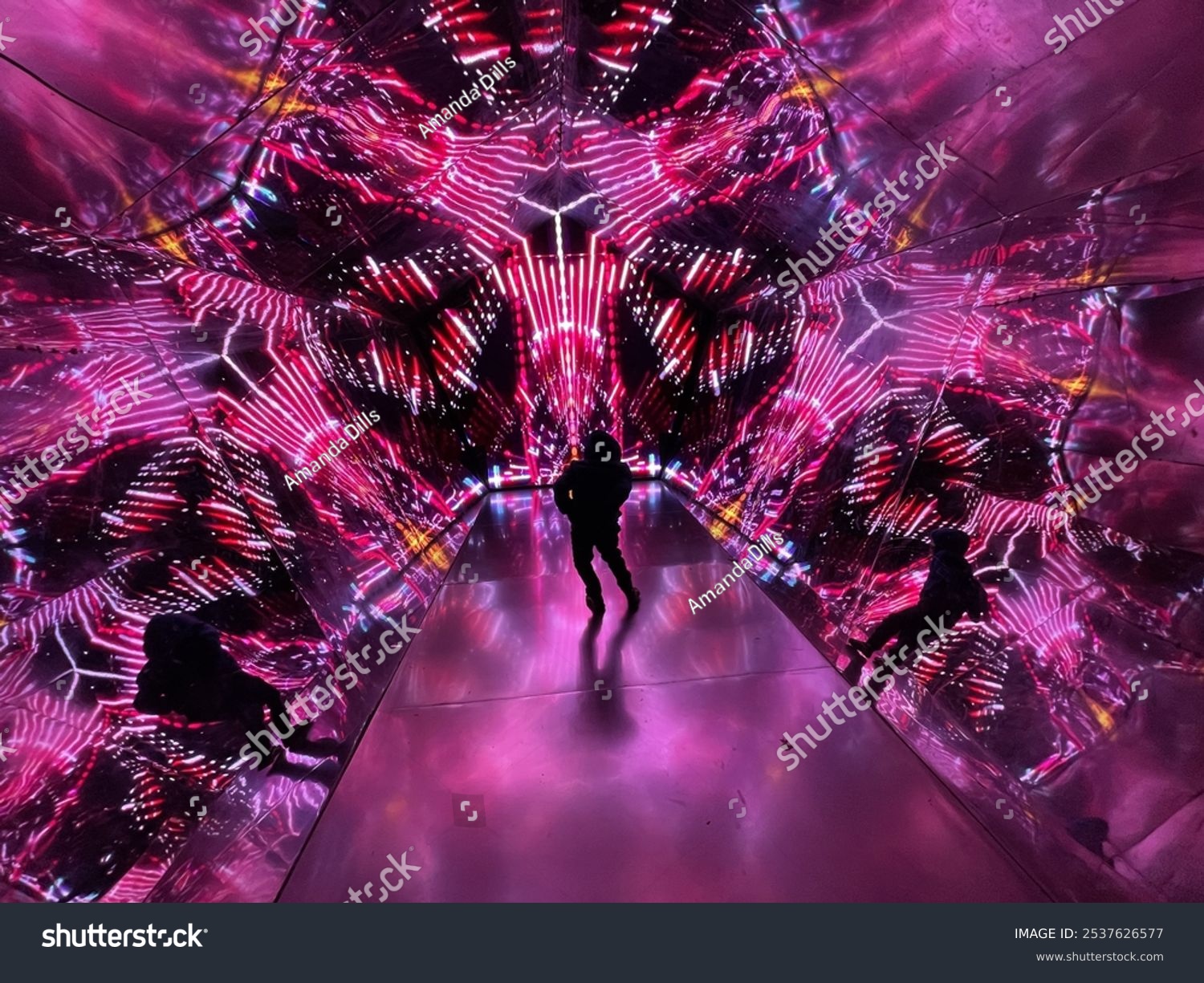 Silhouetted figure in a vibrant mirrored tunnel with neon pink and purple lights creating a kaleidoscopic effect. Perfect for futuristic sci-fi or immersive art themes.