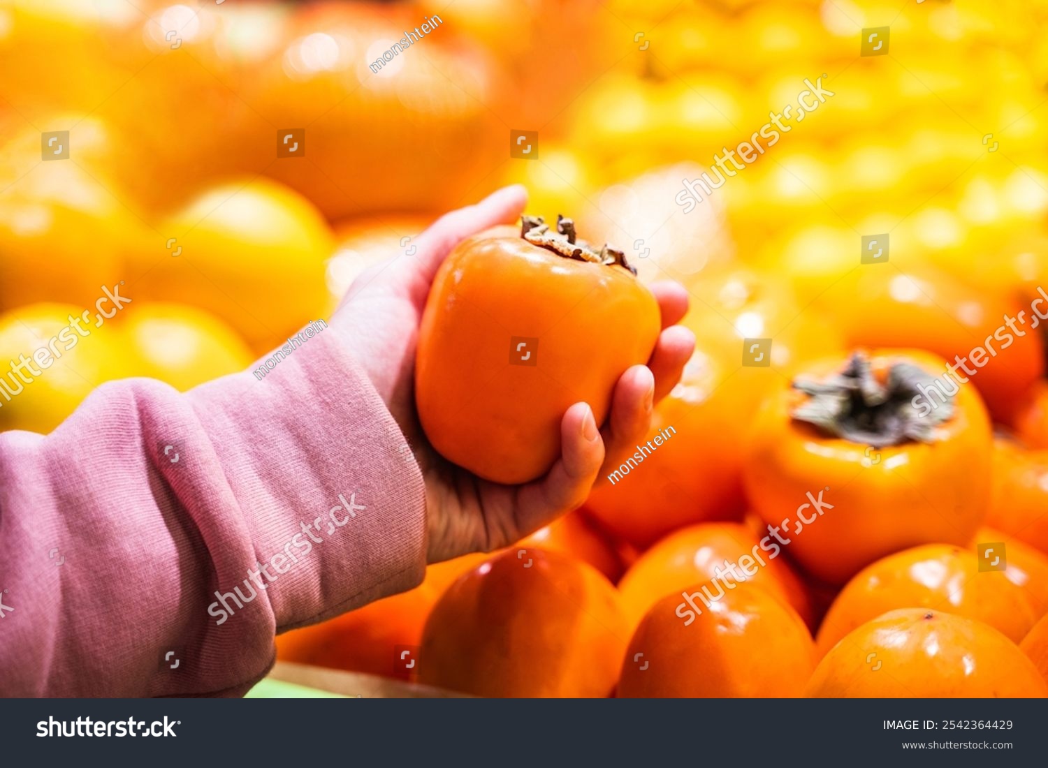 Woman holding fresh persimmon near fruit counter at market  closeup of female hand picking fresh persimmon at supermarket  grocery shopping concept