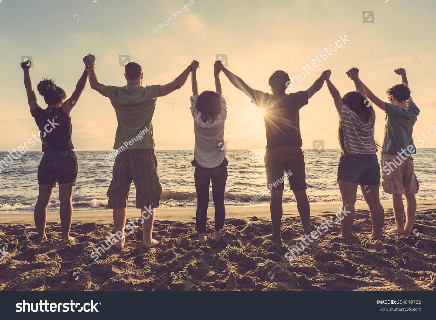 Multiracial group of people with raised arms looking at sunset. Backlight shot. Happiness  success  friendship and community concepts.
