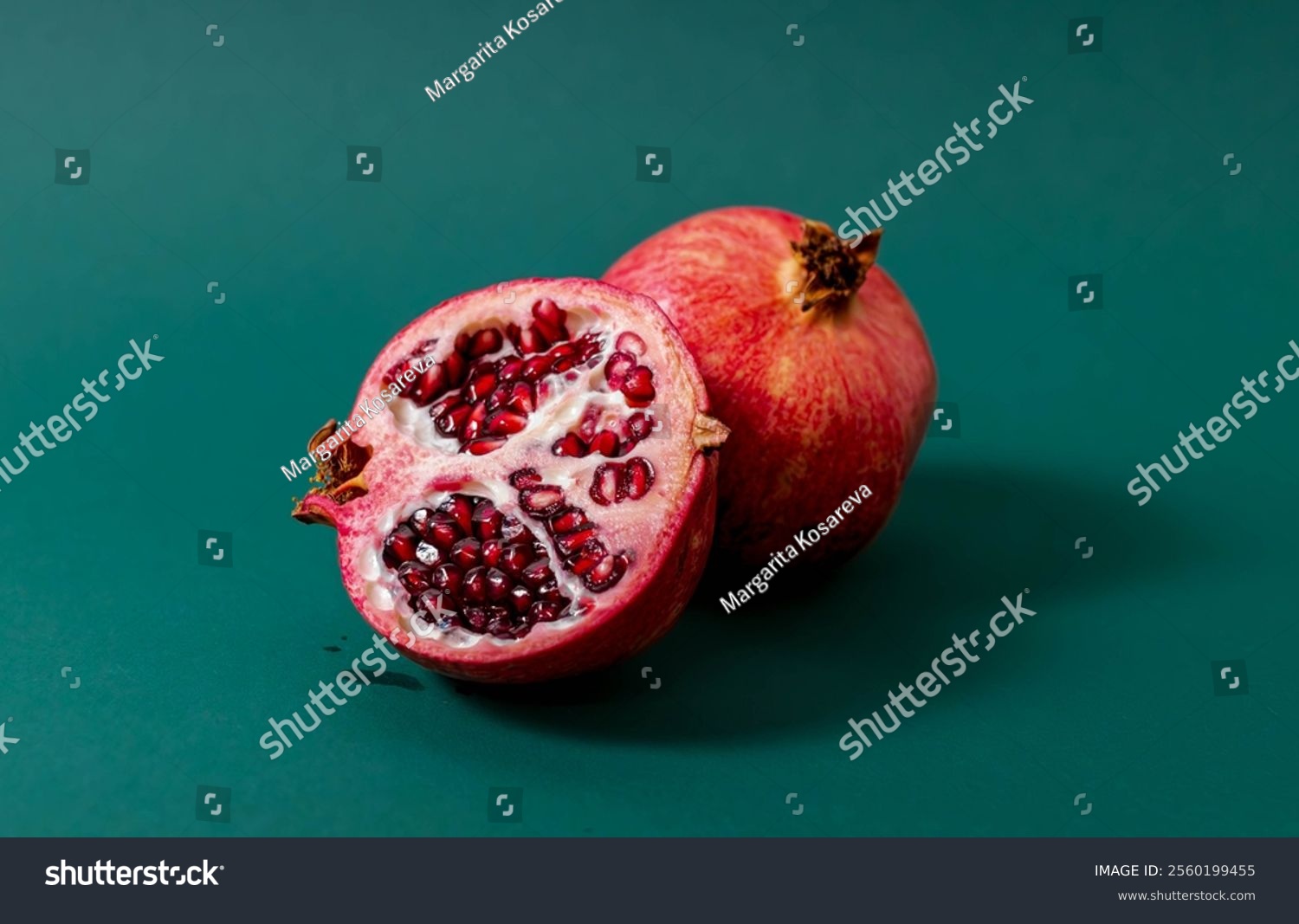 Whole and cut pomegranate with red juicy seeds displayed on a green surface. High-quality horizontal food image for health and nutrition concepts
