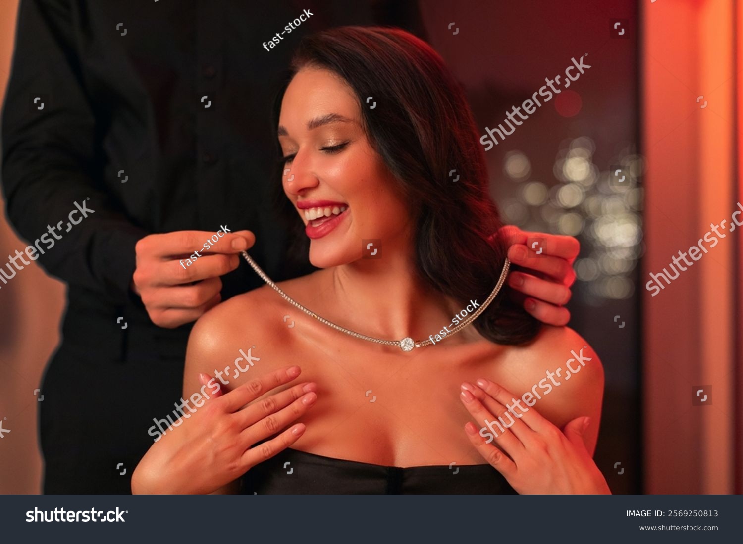 Valentine's gift. Caring man giving luxury necklace to beloved girlfriend  putting it on her neck during romantic date in restaurant