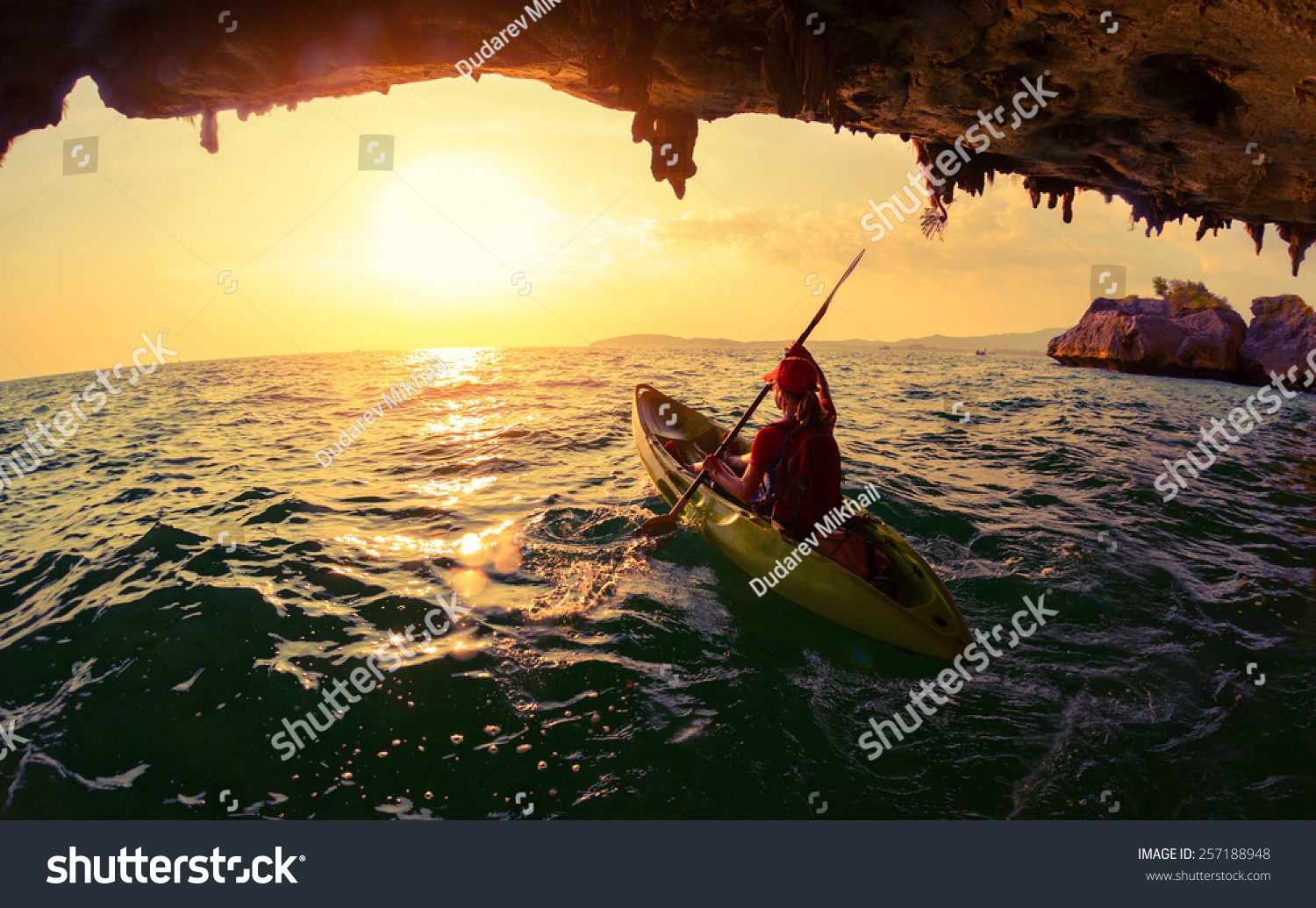Young lady paddling the kayak from limestone cave towards open sea