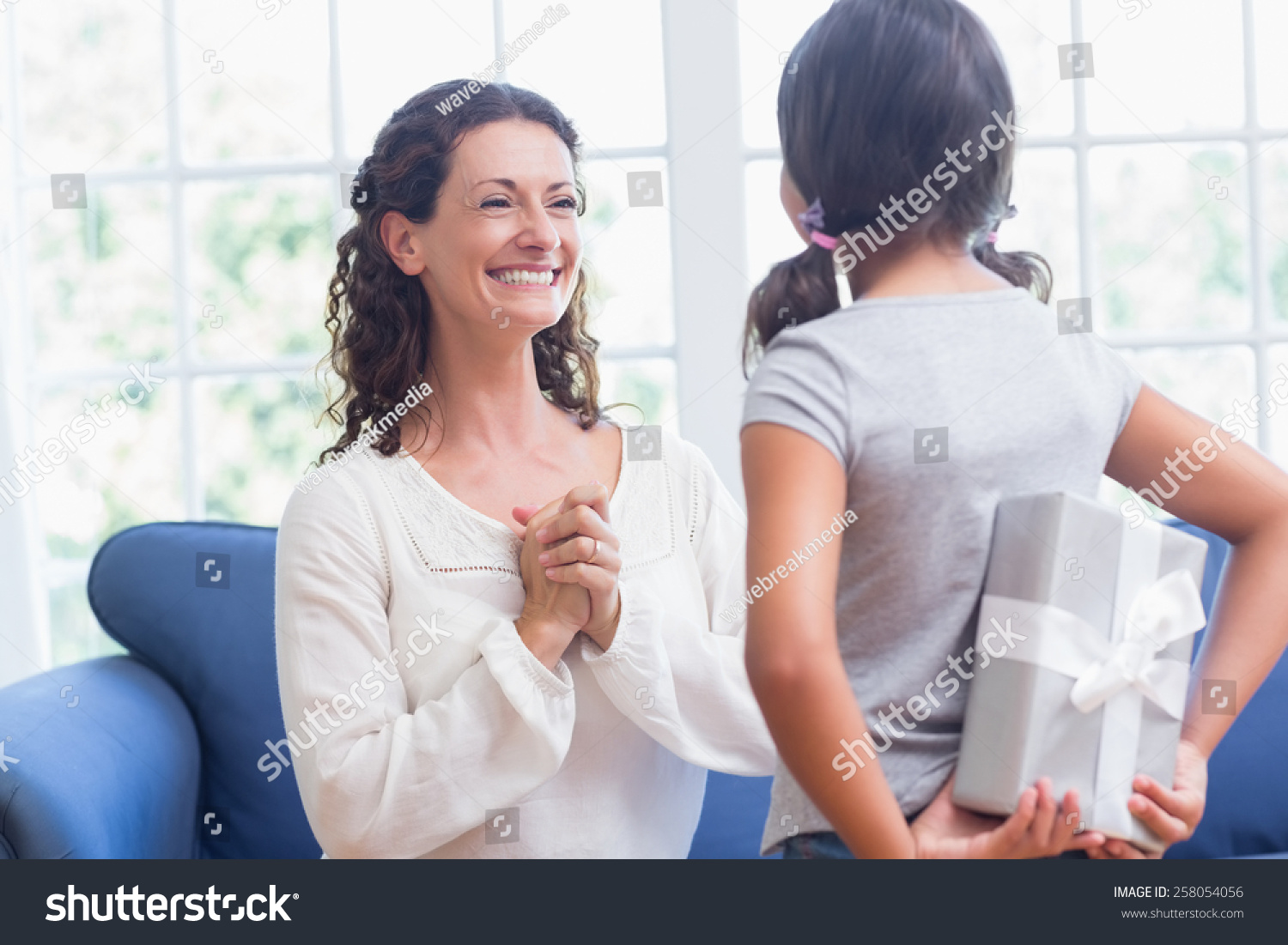 Cute girl offering gift to her mother in the living room