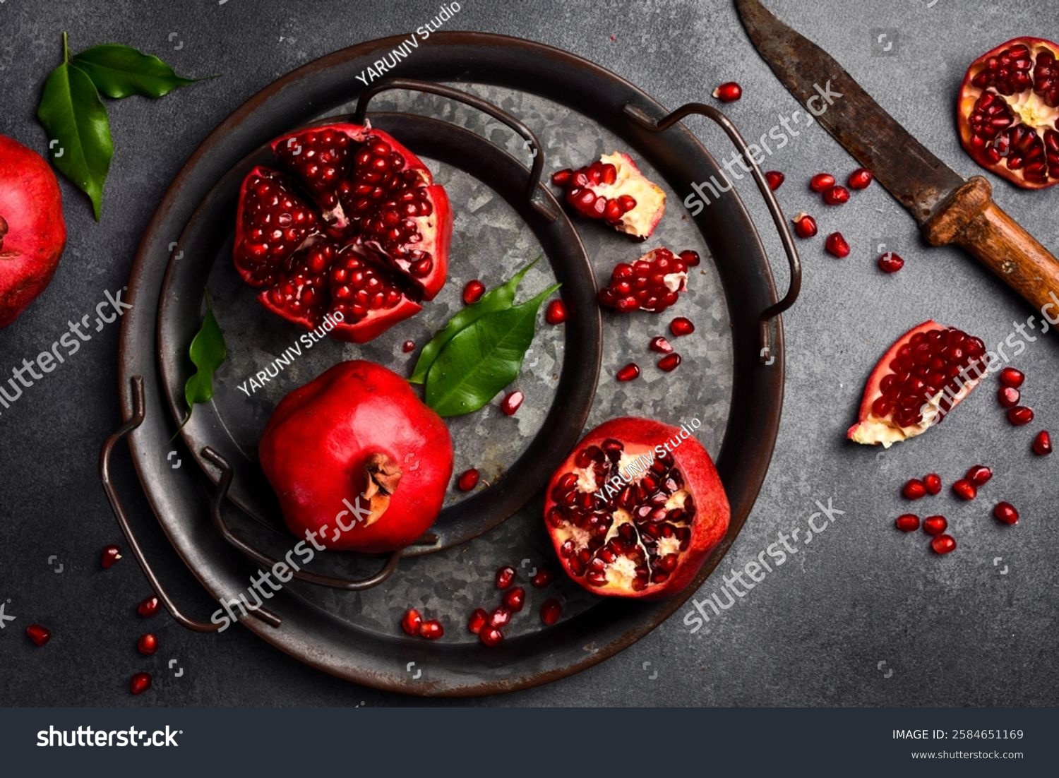 Metal tray with ripe red pomegranates and pomegranate seeds. On a dark background. Close up.