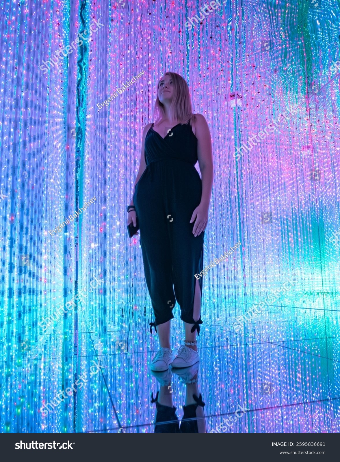 Young woman stands surrounded by colorful lights in an immersive art installation.