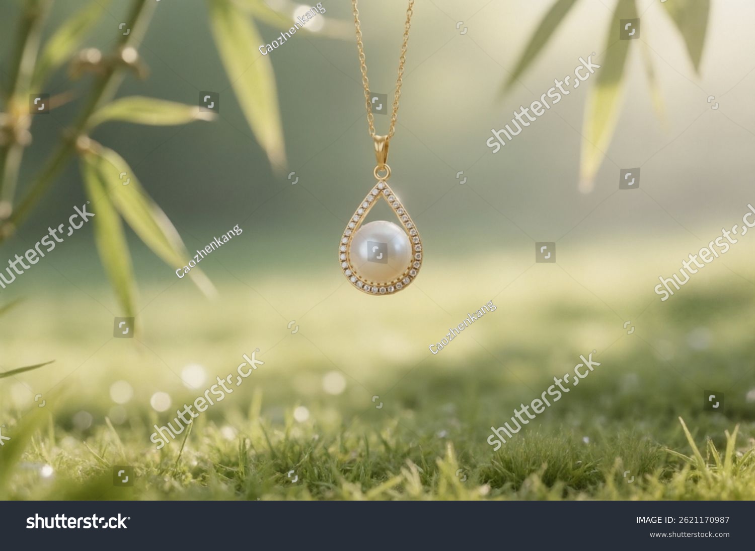 A necklace with a single pearl pendant is suspended in front of the camera lens  with a soft-focus lawn bathed in morning light in the background.