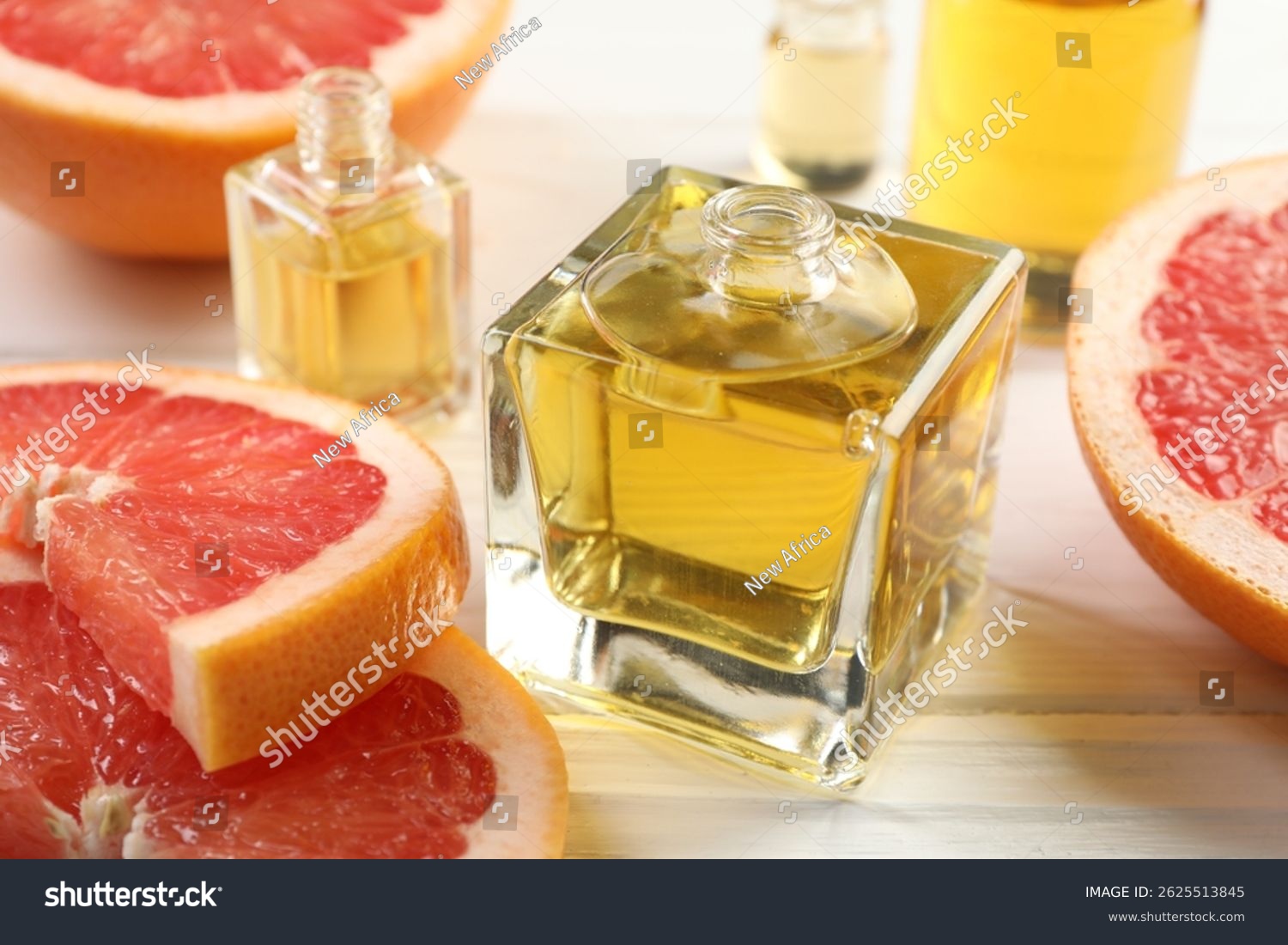 Open perfume bottles with aromatic essential oils and slices of grapefruit on white wooden table  closeup