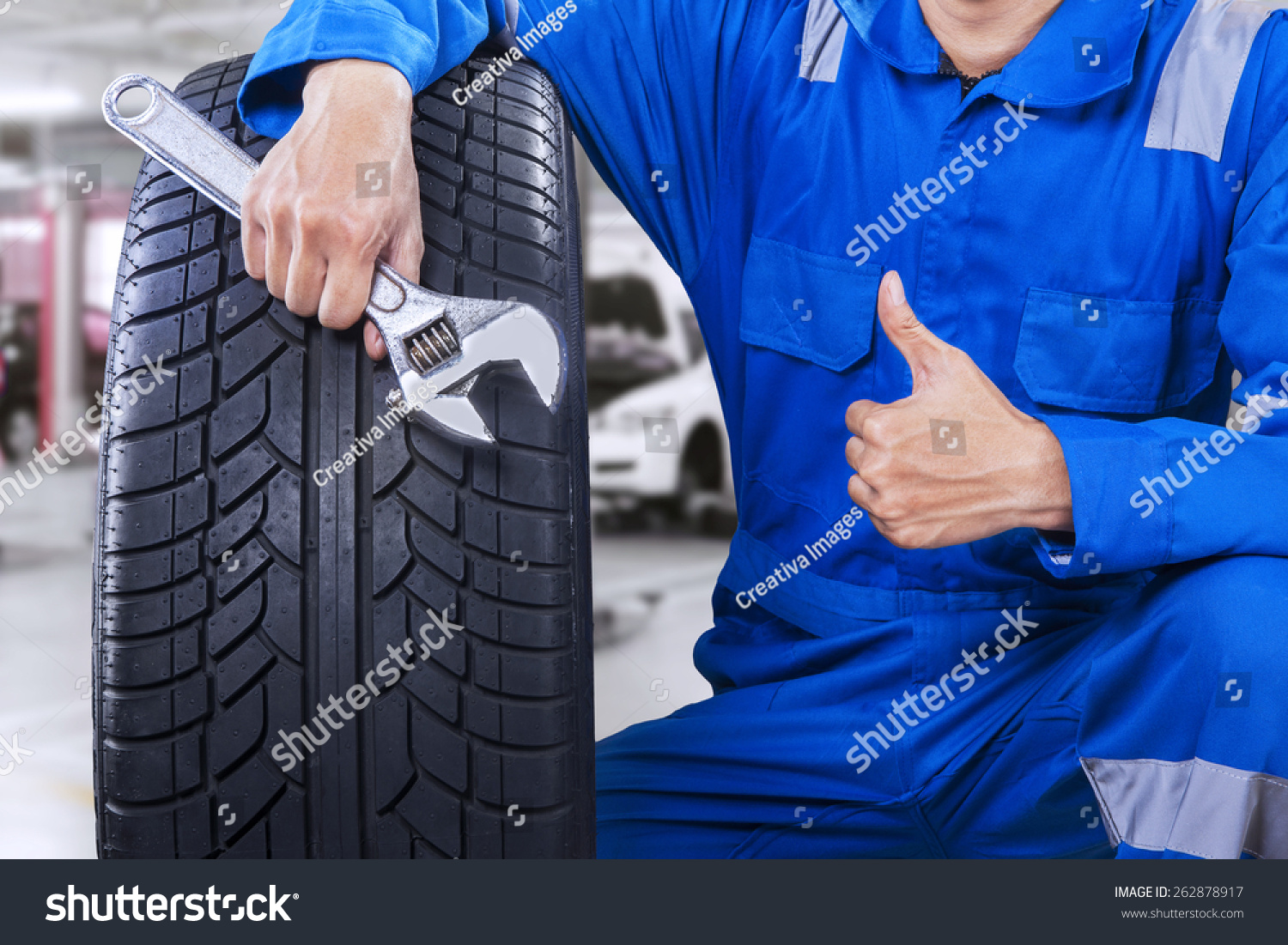 Technician with a blue workwear  holding a wrench and a tire while showing thumb up