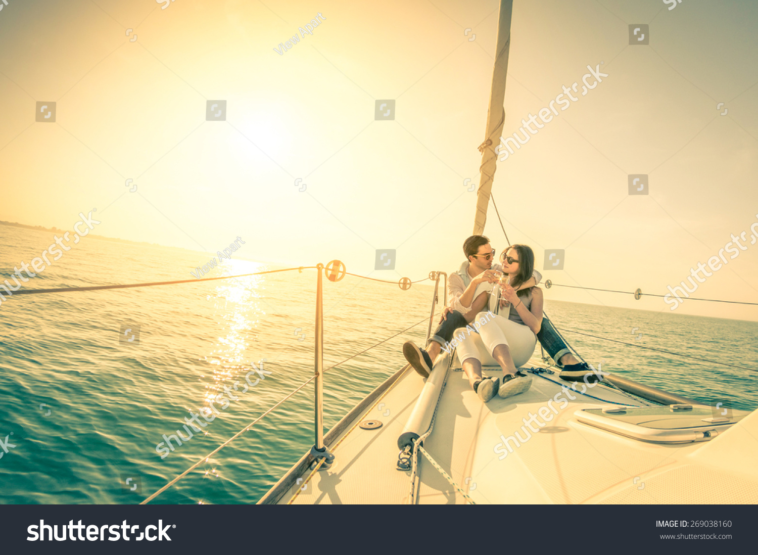 Young couple in love on sail boat with champagne at sunset - Happy exclusive alternative lifestyle concept - Soft focus due to backlight on vintage nostalgic filter - Fisheye lens and tilted horizon