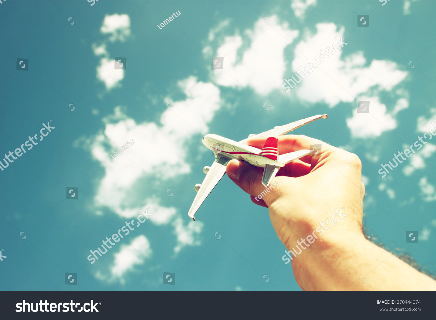 close up photo of man's hand holding toy airplane against blue sky with clouds. filtered image 