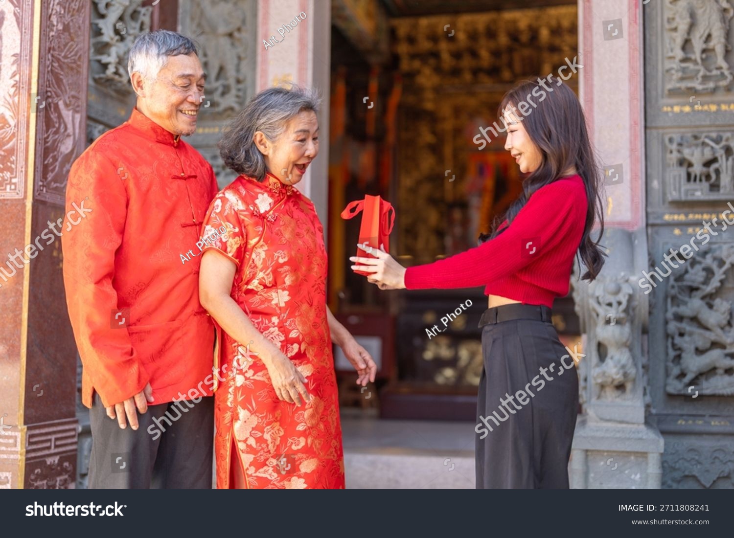 Asian grandparents receiving red envelope from young woman at chinese temple  joyful moment of giving during lunar new year celebration  showing love  family connection and festive cultural tradition