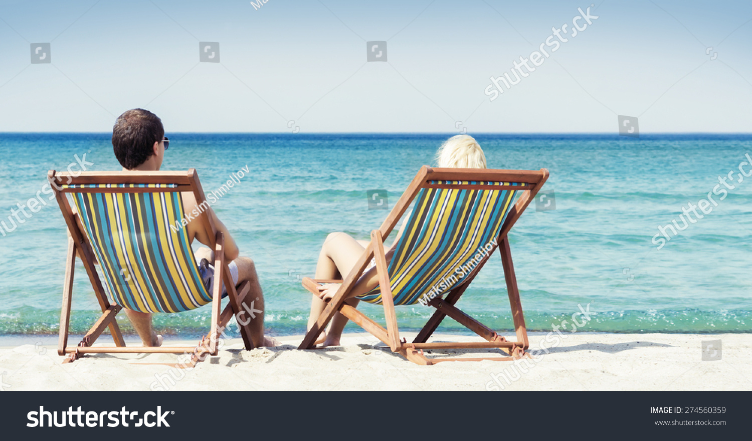 Young couple sitting in a beach chairs and looking at the sea