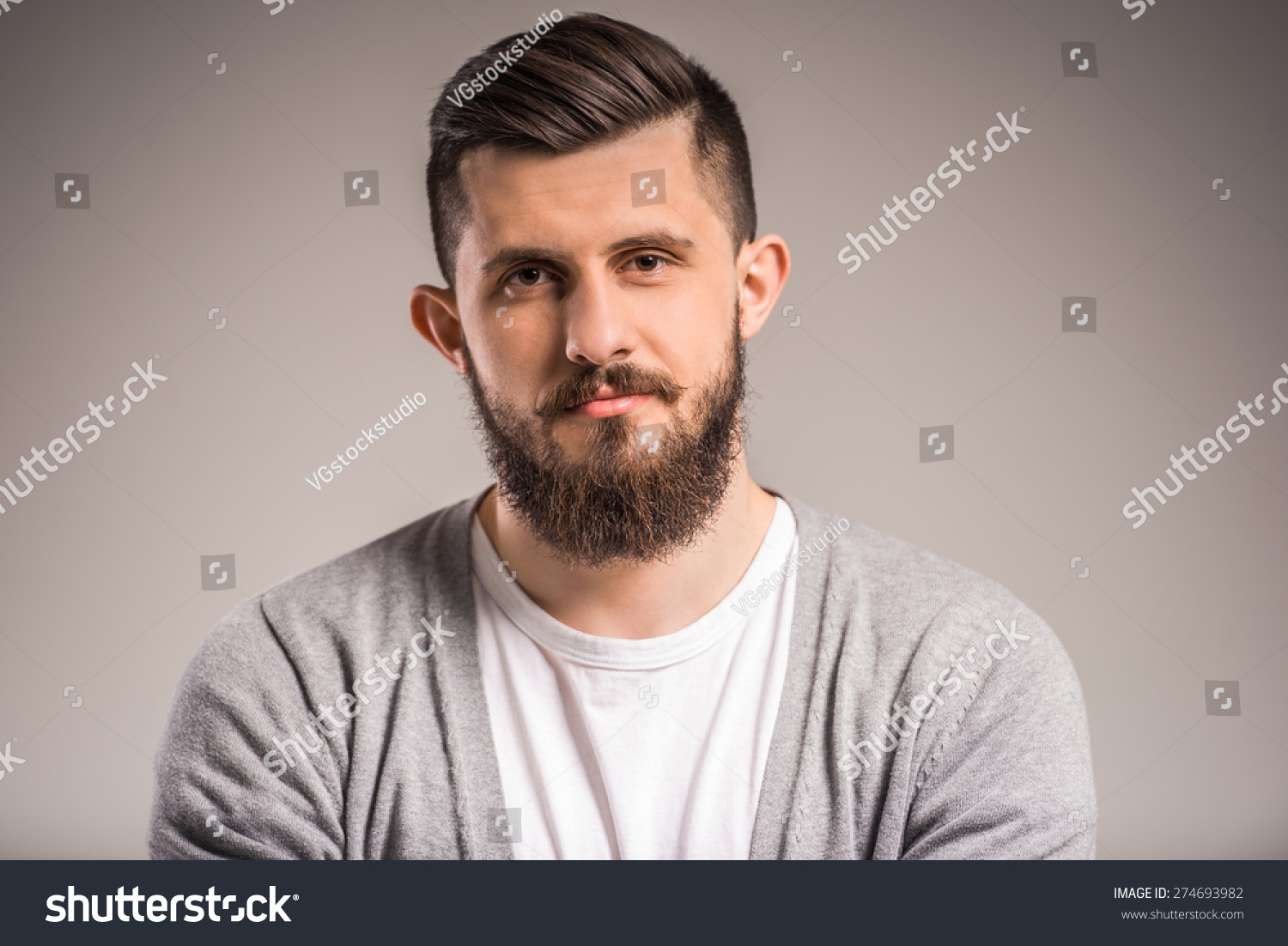 Confident bearded man is looking at the camera  standing on gray background.