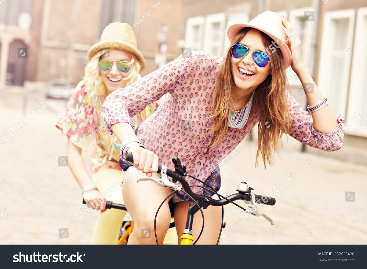 A picture of two girl friends riding a tandem bicycle in the city