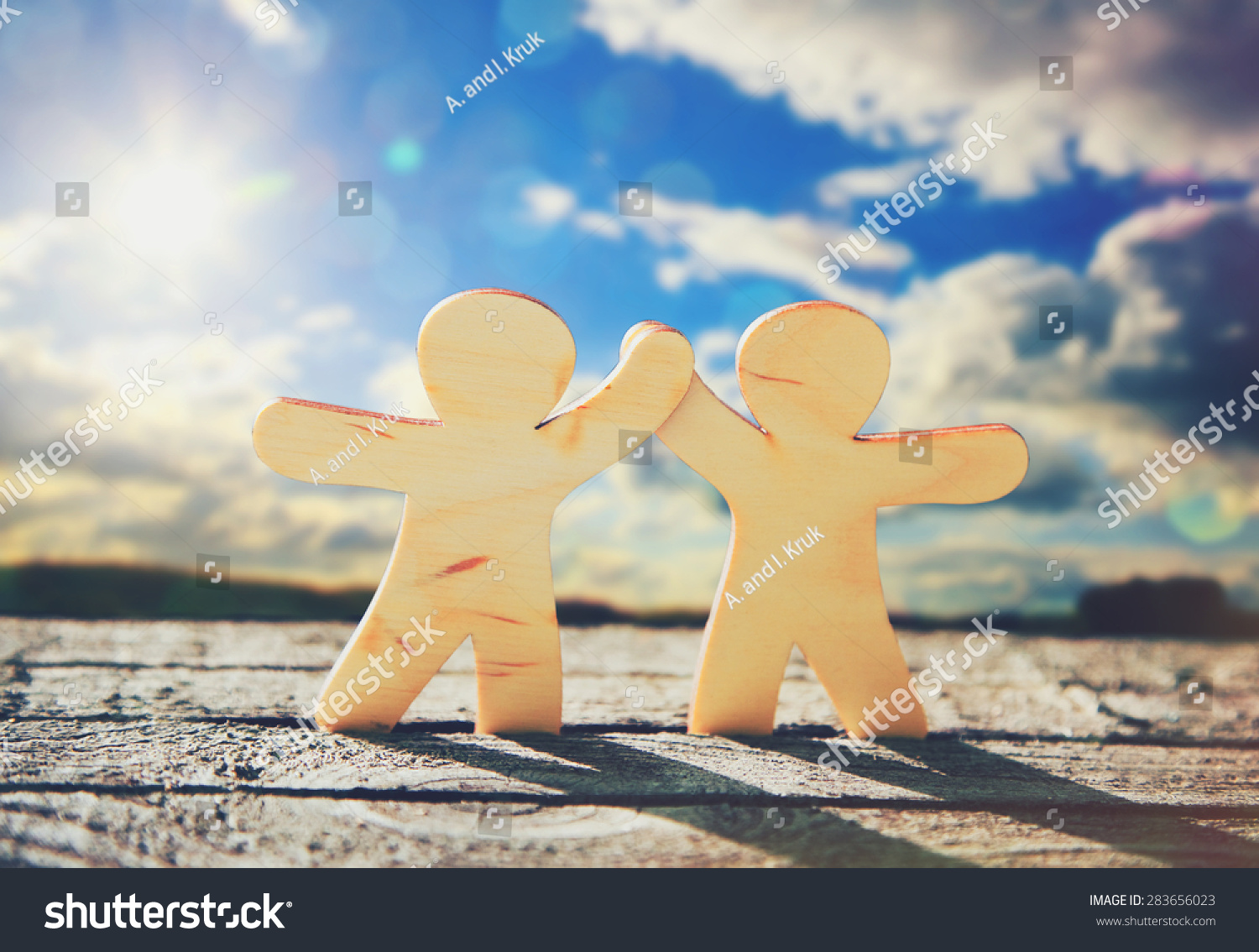 Wooden little men holding hands on sky and sun background. Symbol of friendship love and teamwork