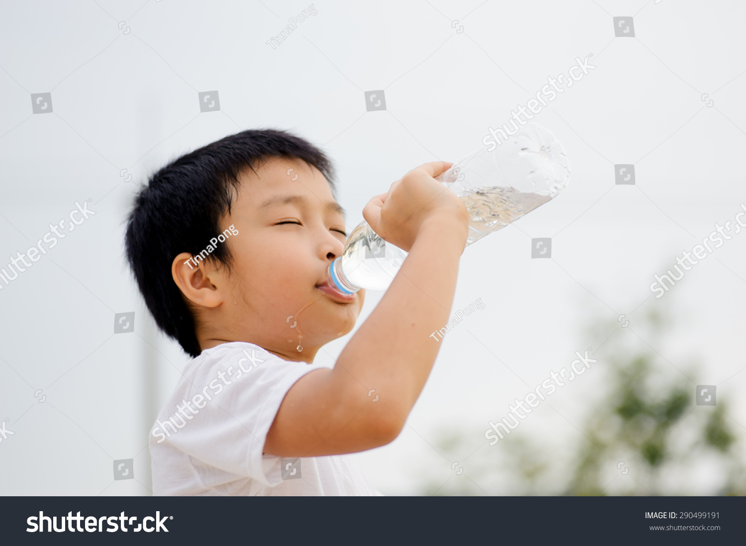 Asian young boy drinking fresh water from plastic bottle after sport in daylight