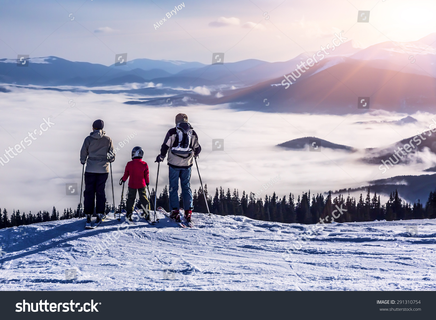 People observing mountain scenery.
Family of three people stays in front of scenic landscape. These are skiers they dressed in winter sport jackets and have skies attached.
