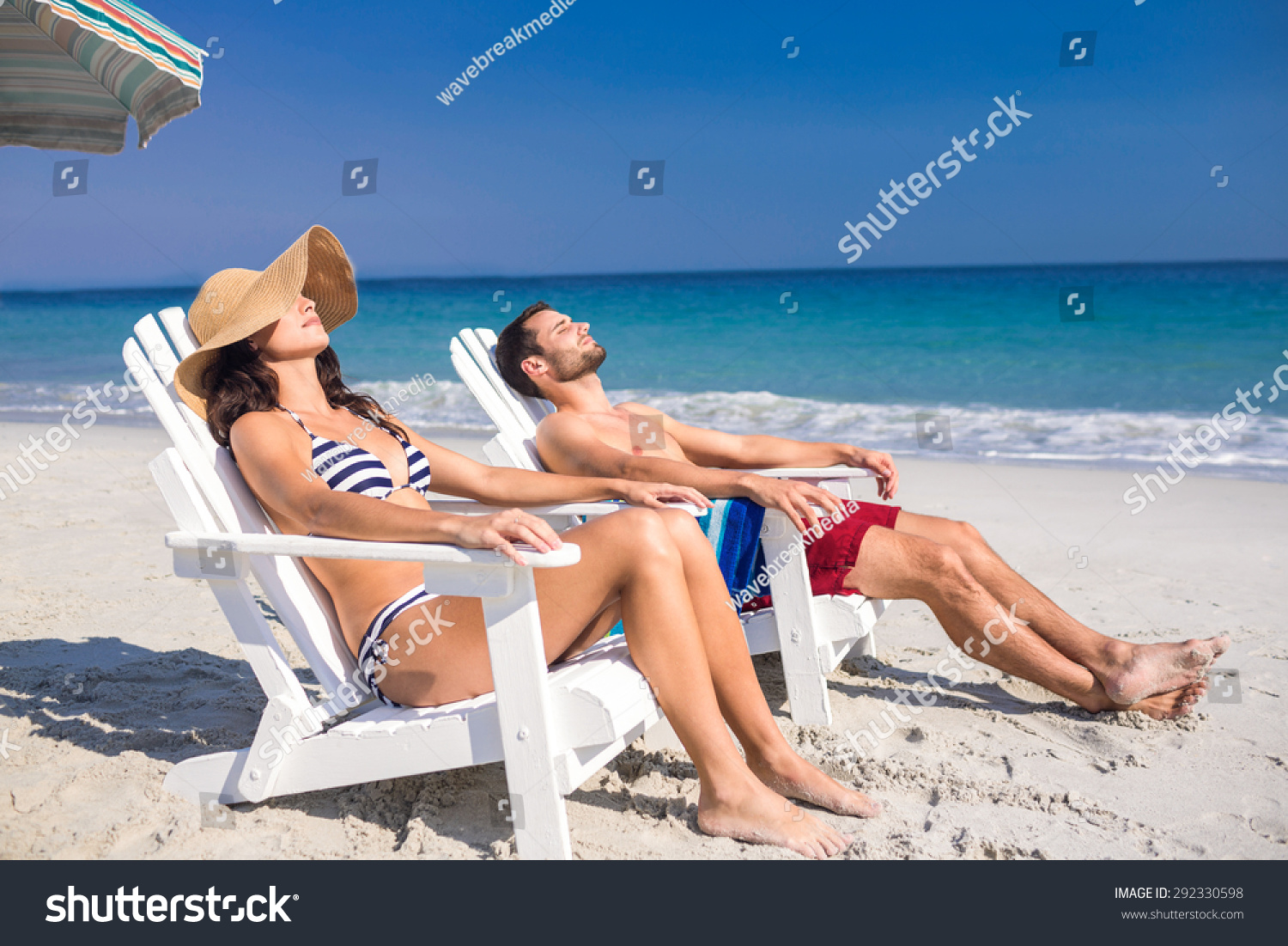 Happy couple relaxing on deck chair at the beach on a sunny day