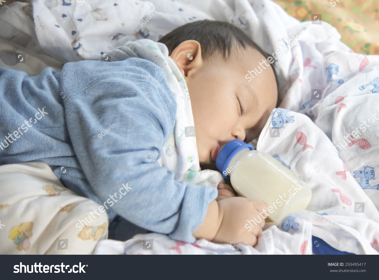 Cute and adorable Asian baby sleeping and drinking milk from the bottle alone on the bed