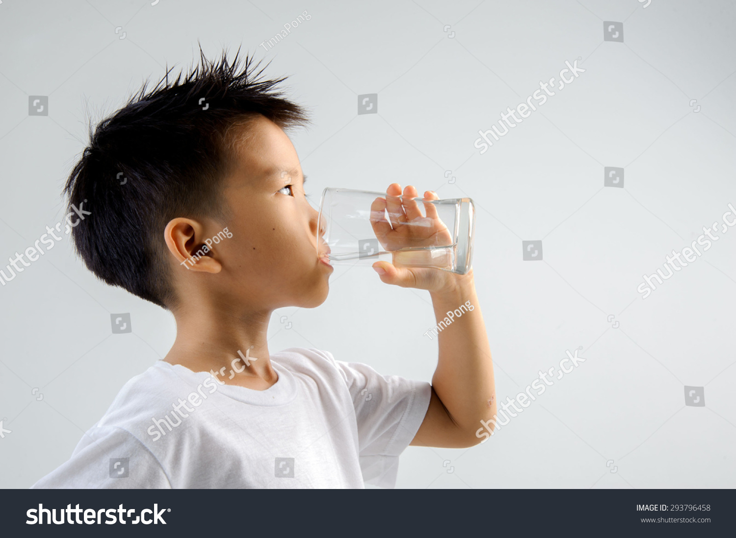 Asian young boy in white shirt hold glass of fresh water in hand and drink. Concept water day.