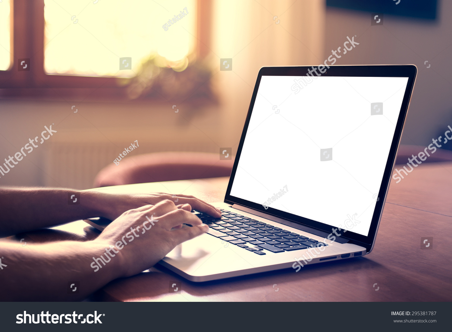 Man's hands using laptop with blank screen on desk in home interior.