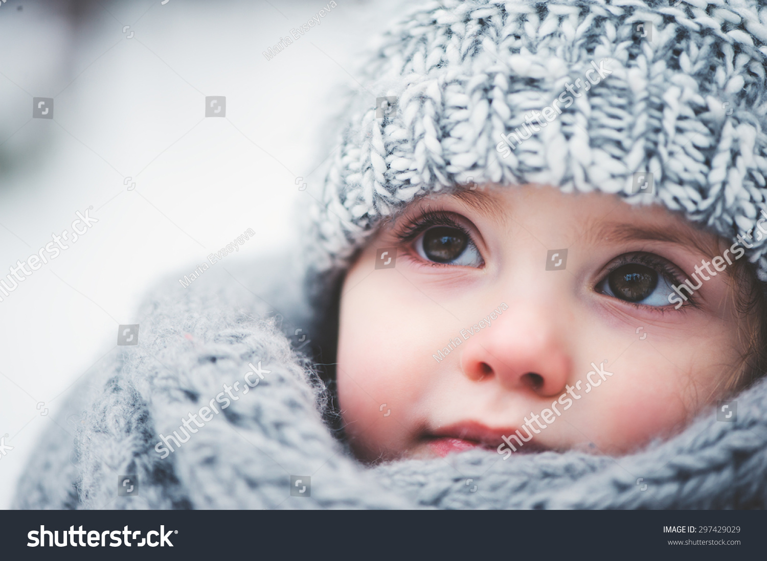 winter close up outdoor portrait of adorable dreamy baby girl in grey knitted hat and scarf