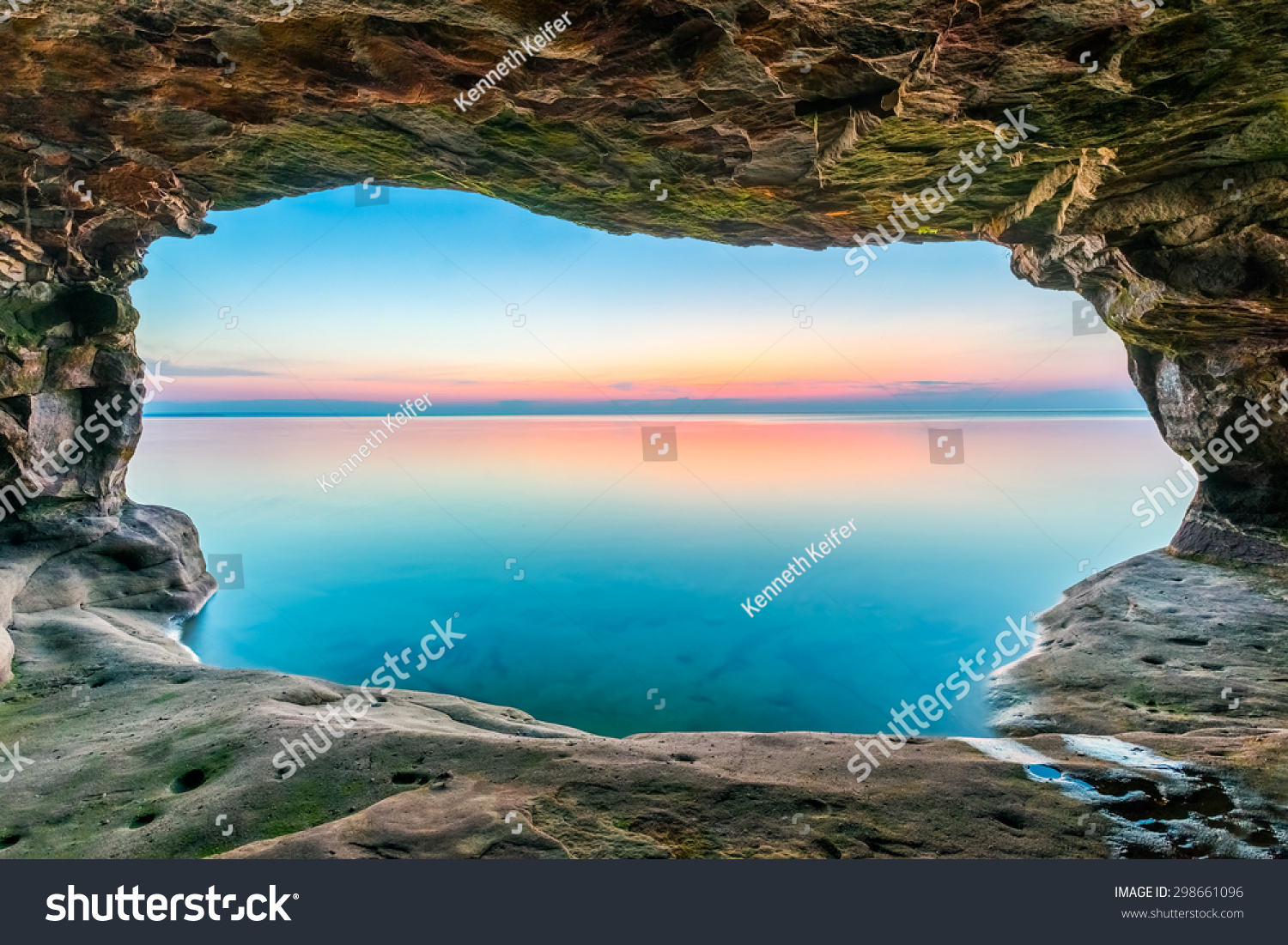A sunset sky  reflected upon a calm Lake Superior  is framed by a sea cave along the Upper Peninsula coastline of Michigan.
